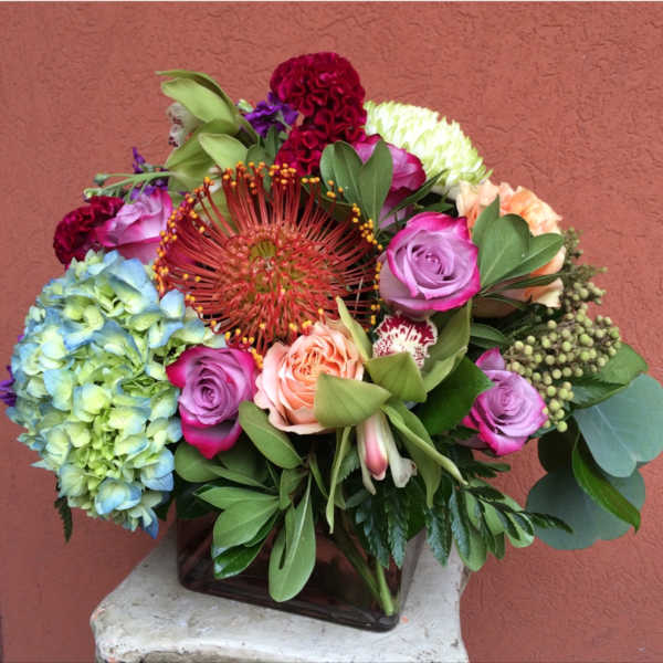 Mixed bouquet with roses, hydrangea, and a large red pincushion bloom in a square vase