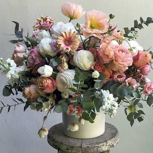 Mixed bouquet of peach, pink, and white flowers in a white vase