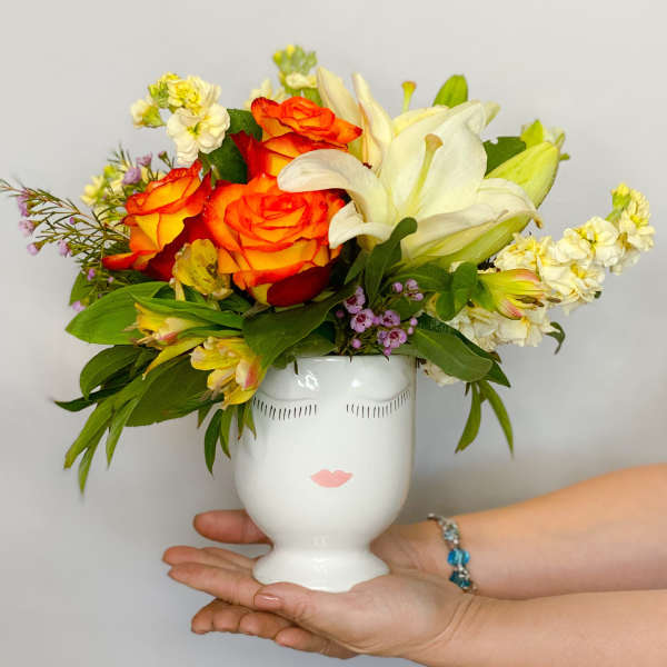 Bouquet of orange roses and white lilies in a white face vase