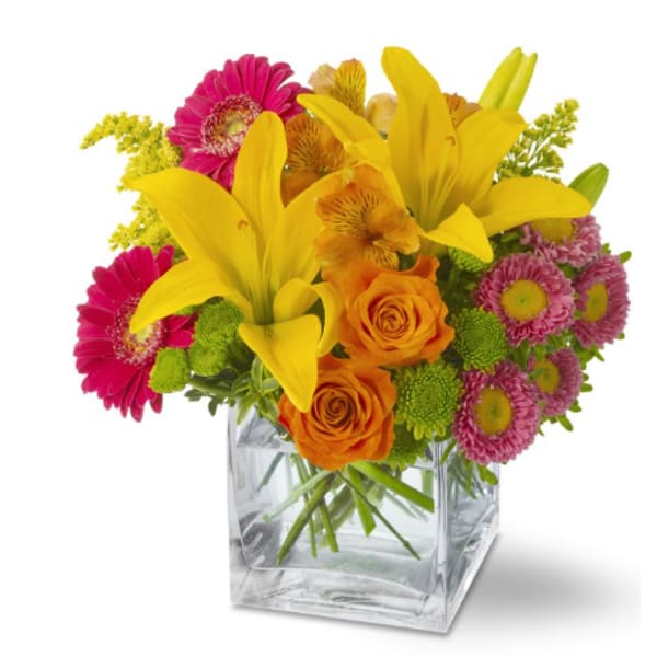 Yellow lilies, orange roses, and pink daisies in a clear square vase