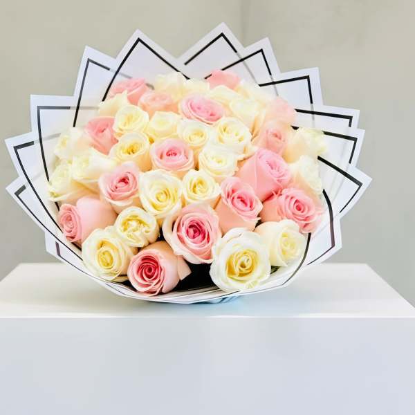 Round bouquet of cream and soft pink roses wrapped in layered white paper with black trim