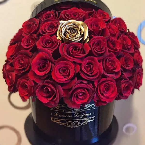 Round box of red roses with one gold rose in the center