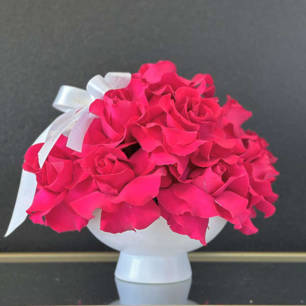 Bright pink rose bouquet in a white vase with a ribbon bow