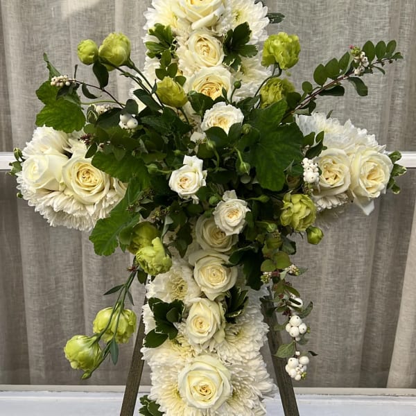 White floral cross on an easel with roses and chrysanthemums