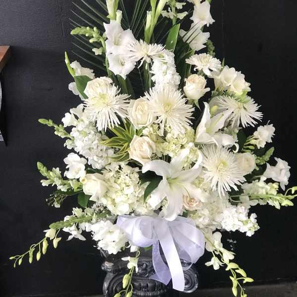 White floral arrangement in a dark vase with a lavender ribbon