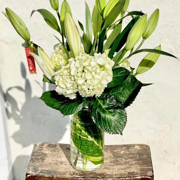 White hydrangeas and unopened lilies in a glass vase
