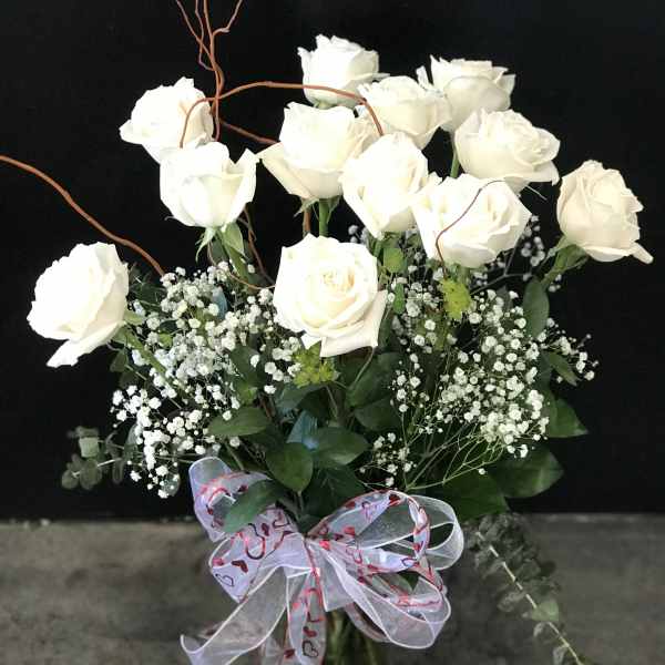 White roses arranged in a glass vase with baby's breath and a heart ribbon