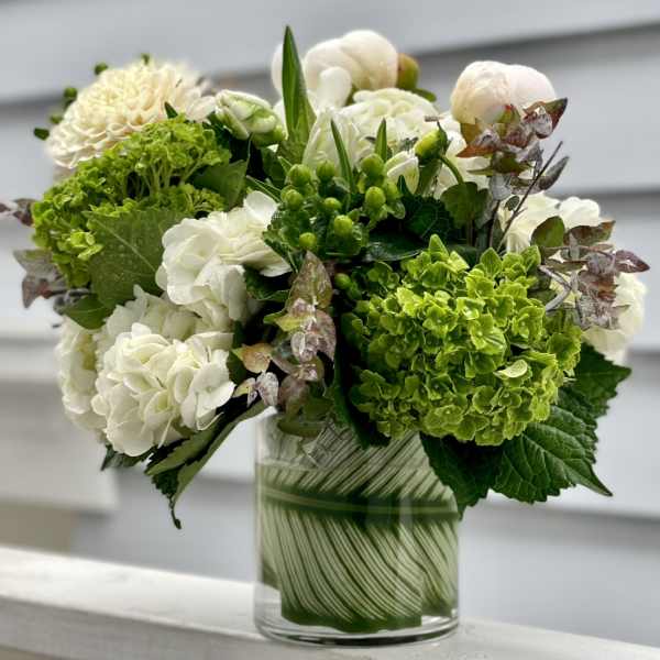 Compact arrangement of white and green blooms in a clear glass cylinder vase