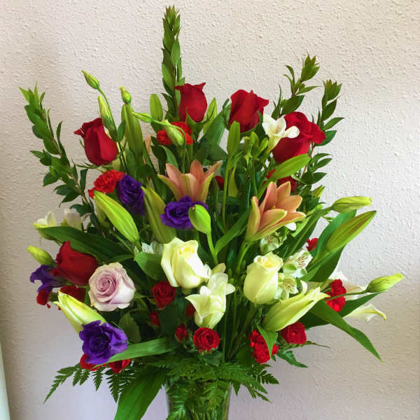 Tall mixed bouquet of roses, lilies, and orchids in a clear glass vase