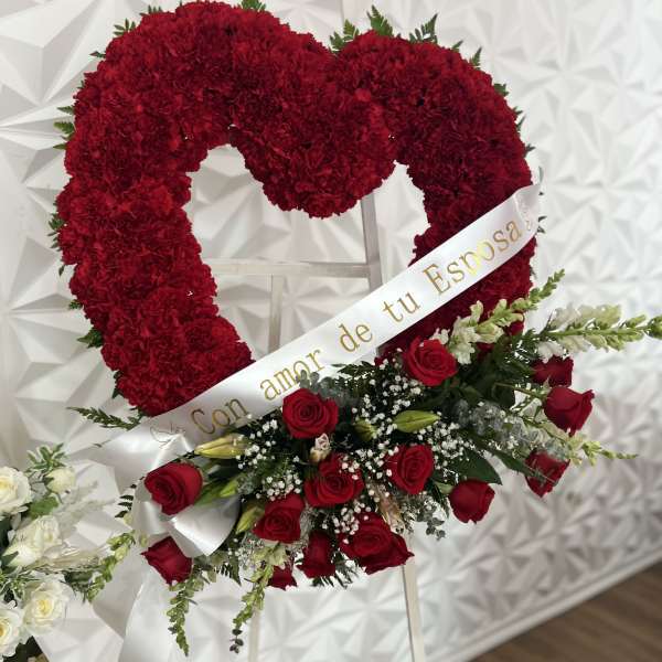 Heart-shaped red floral wreath with roses and a white ribbon on an easel