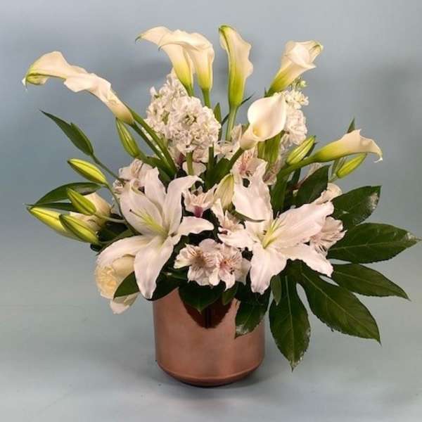 White calla lilies and pale pink flowers arranged in a copper vase