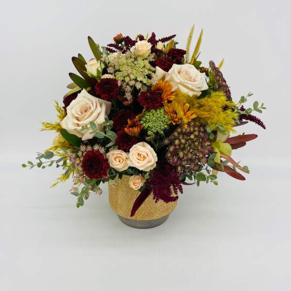 Low arrangement of cream roses and burgundy mums with golden accents in a gold ceramic vase