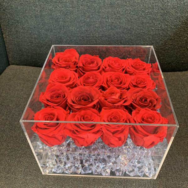 Red roses arranged in a clear square acrylic box with crystal filler