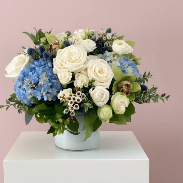White roses and blue hydrangeas arranged in a white vase