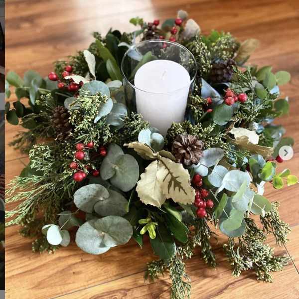 Candle in a glass holder surrounded by a holiday greenery wreath
