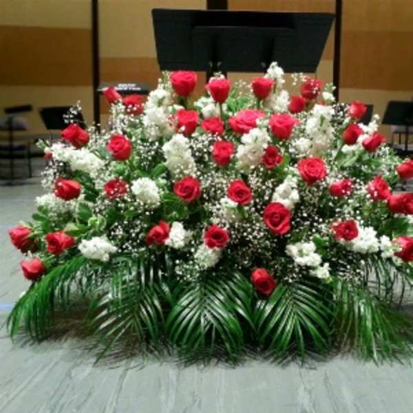 Large fan-shaped arrangement of red roses and white flowers with palm fronds on a stage.