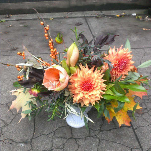 Low arrangement of peach dahlias and amaryllis with orange berries in a white vase