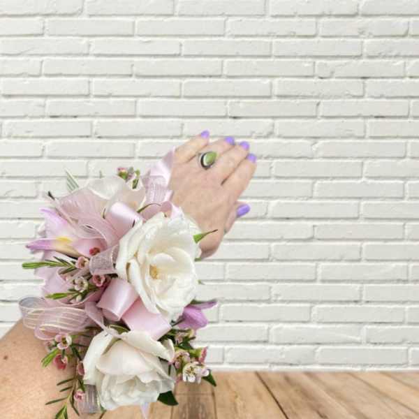Pink and white floral wrist corsage with ribbon on a hand