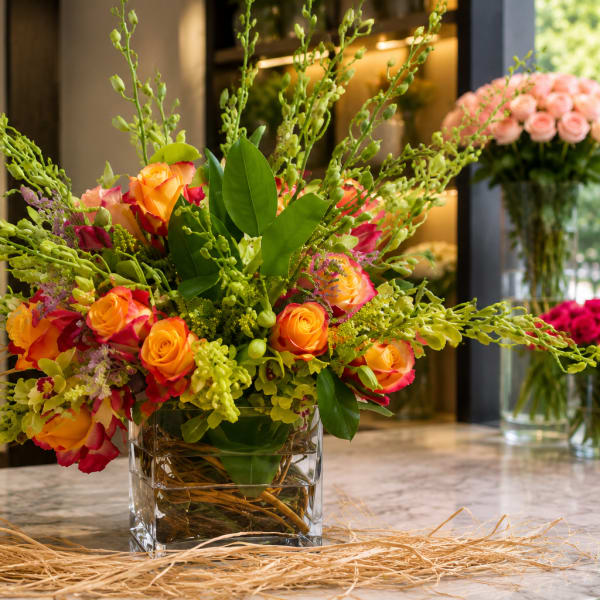 Bright orange and pink rose arrangement in a clear square vase