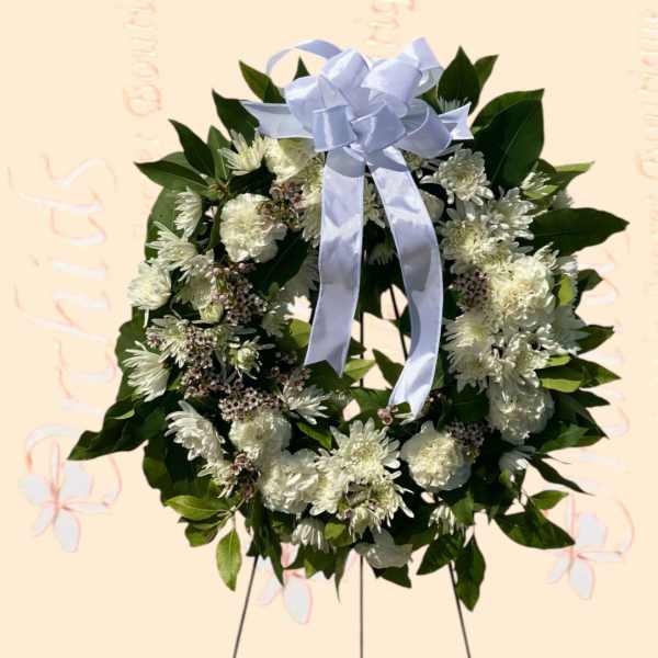 White floral wreath with a pale blue ribbon bow on a stand