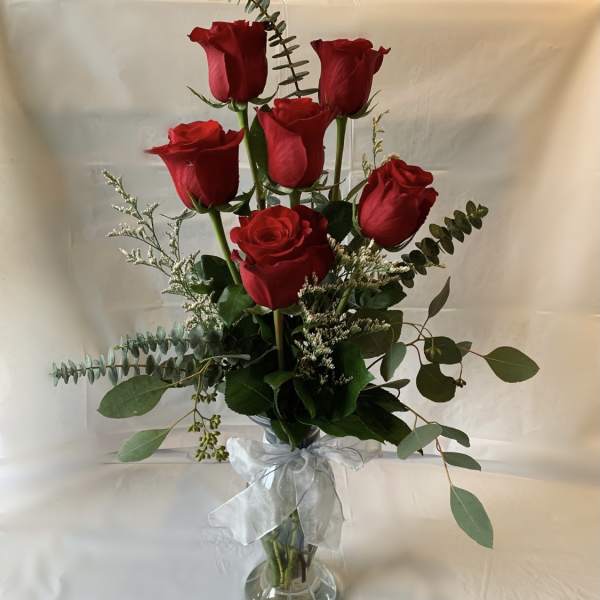 Red roses arranged in a clear glass vase with a white ribbon
