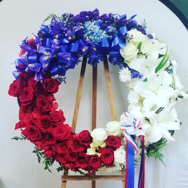 Circular floral wreath with red, white, and blue flowers on a wooden stand