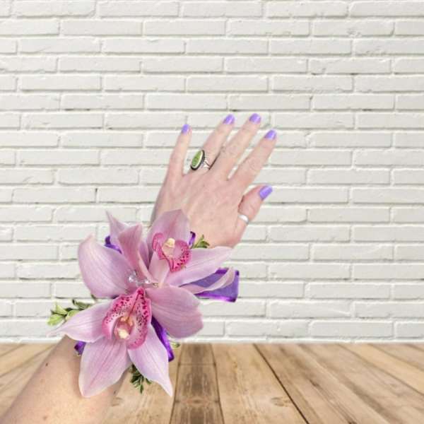 Pink orchid corsage on a wrist with purple ribbon
