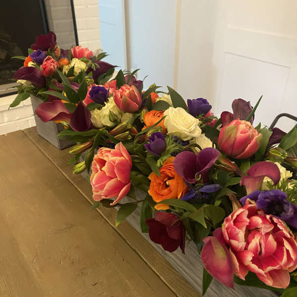 Long low floral arrangement with tulips, roses, calla lilies, and purple blooms