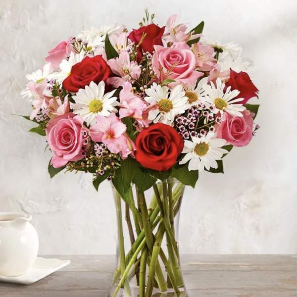 Bouquet of red and pink roses with white daisies in a clear glass vase
