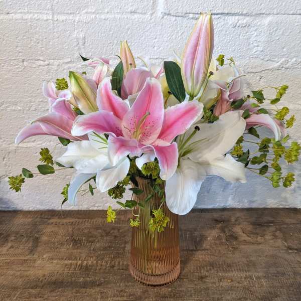 Pink and white lilies arranged in a ribbed glass vase