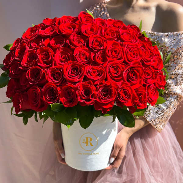 Large round arrangement of red roses in a white hatbox held by a person in a sequin dress