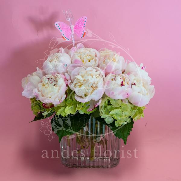 Pink and white peonies in a clear glass vase with a butterfly pick