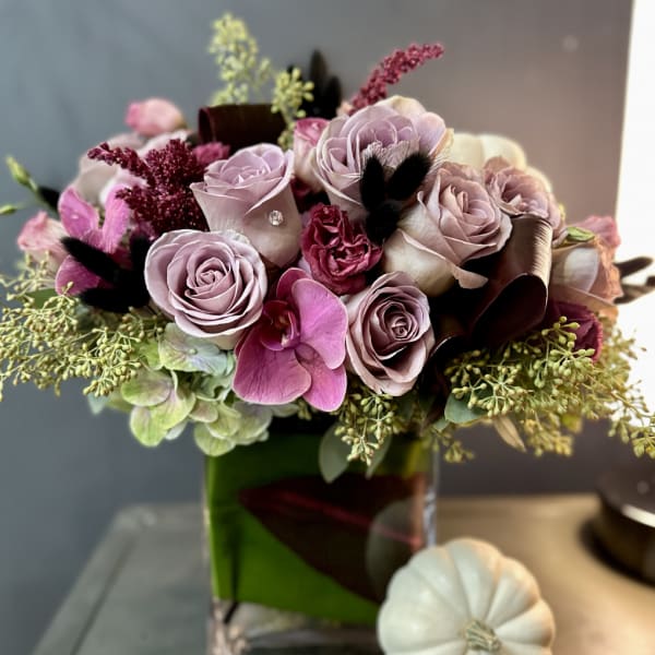 Pink and lavender rose bouquet in a green glass vase with a white pumpkin