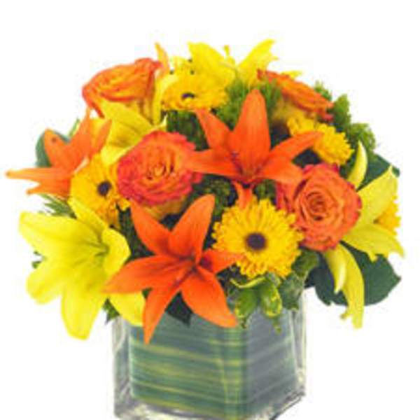 Orange and yellow flowers arranged in a clear square vase