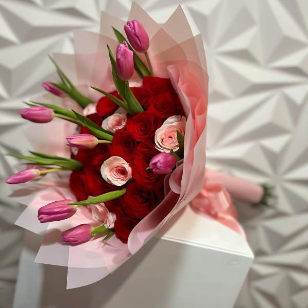 Bouquet of red roses and pink tulips wrapped in pale pink paper