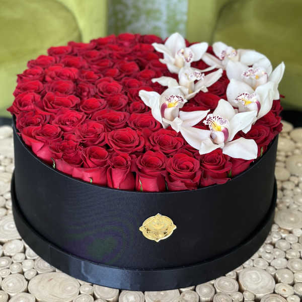Round box of red roses topped with white orchids