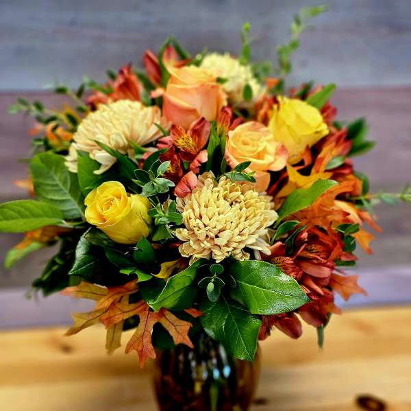 Bouquet of yellow and peach roses with orange flowers in a dark glass vase
