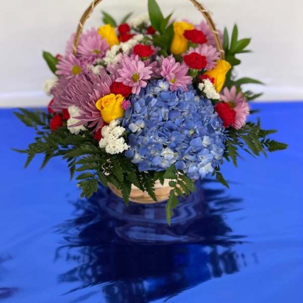 Basket arrangement of blue hydrangeas, pink daisies, and yellow roses