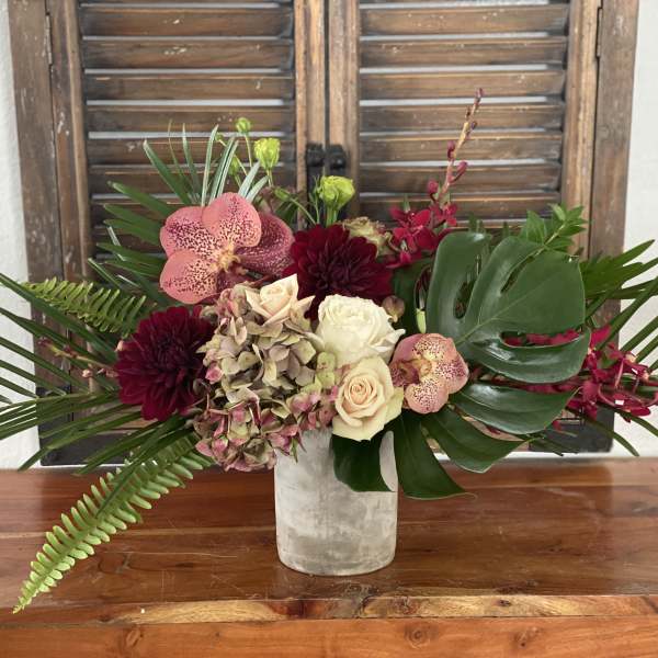 Tropical bouquet with orchids, roses, and dark dahlias in a white vase