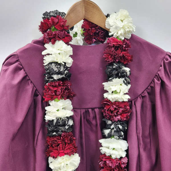 Red, white, and black carnation lei draped over a mauve graduation gown on a wooden hanger