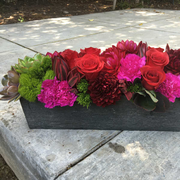 Low rectangular arrangement of red and pink flowers in a dark planter