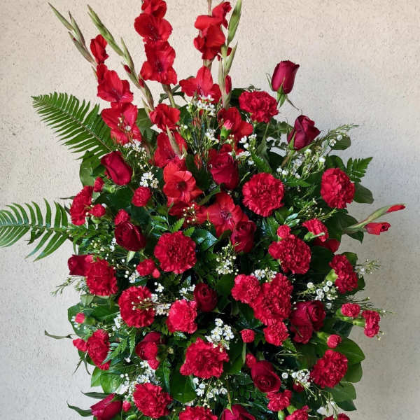 Tall standing spray of red flowers with greenery on a black easel