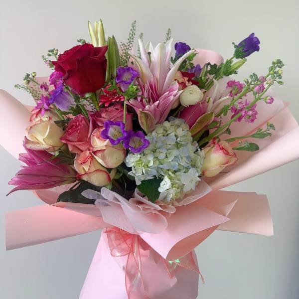 Pink and purple bouquet with roses, lilies, and hydrangea wrapped in pink paper