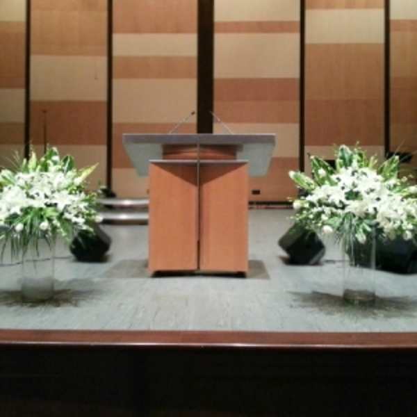 Two large white lily and rose arrangements in clear glass vases on a stage beside a podium