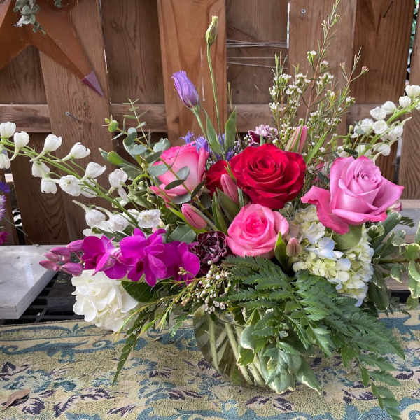 Mixed bouquet of roses, orchids, and white blossoms in a glass vase