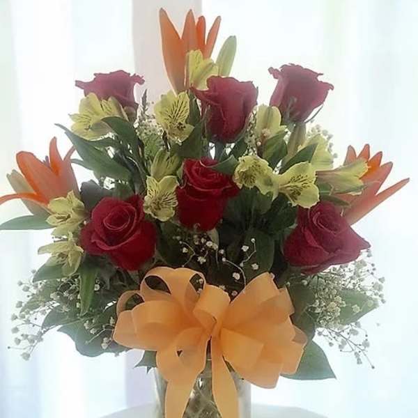 Bouquet of red roses and orange lilies in a glass vase with a bow