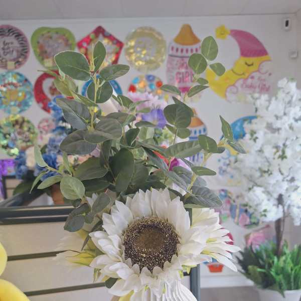 White sunflower arrangement in a ribbed vase with green foliage