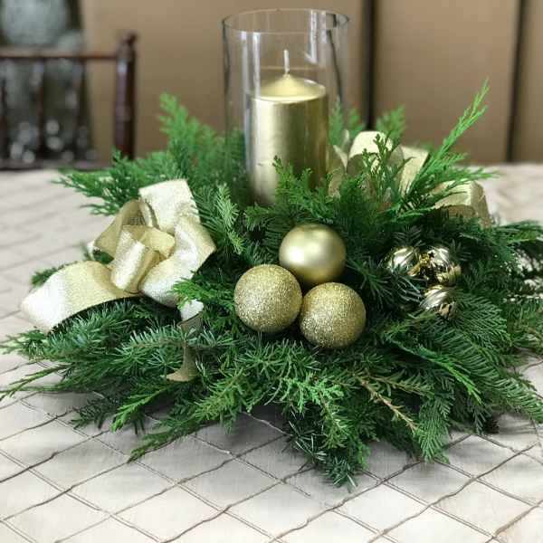 Green holiday centerpiece with gold ornaments and a glass candle holder