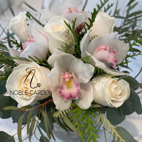 White roses and pink orchids in a bouquet with greenery