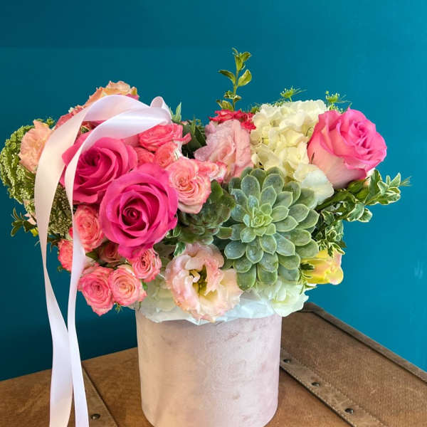 Pink roses and succulents arranged in a pale hatbox with a ribbon